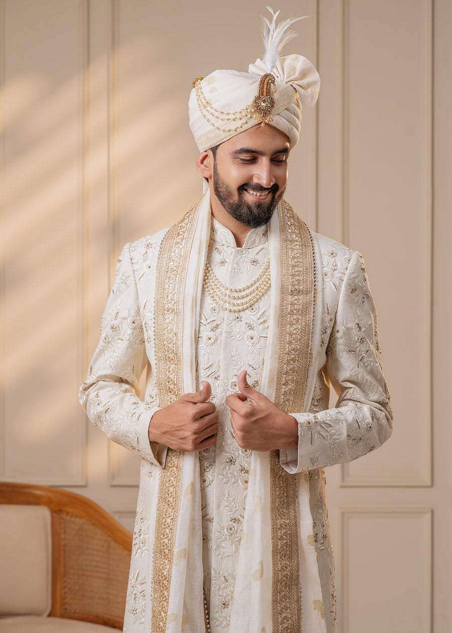 This elegant ivory sherwani set features intricate floral embroidery and zardosi work, perfect for grooms seeking a blend of tradition and style.